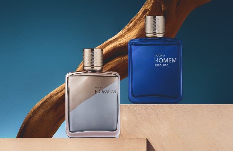 Foto com fundo azul. Dois frascos de perfume Natura Homem e Natura Homem Absoluto sobre blocos de concreto com madeira ao fundo.